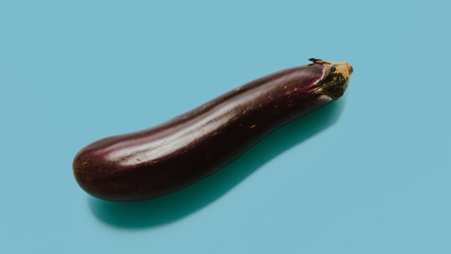 A single aubergine lying on a blue background